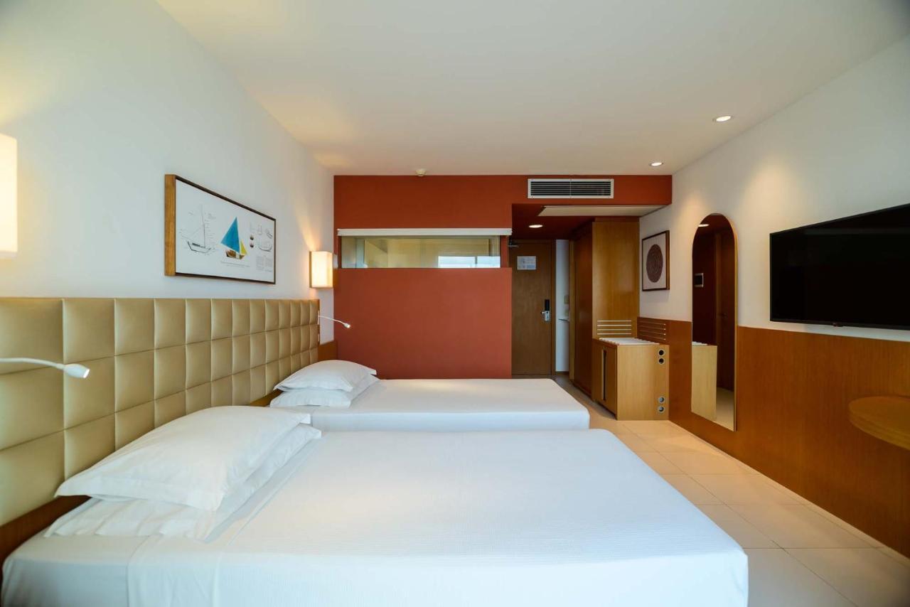 Hotel Luzeiros Sao Luis Экстерьер фото The image shows a modern hotel room featuring two single beds with white bedding. The headboard of the beds is a soft, cream-colored material. The room has a minimalist design with light-colored walls and a contrasting accent wall in a warm orange sh