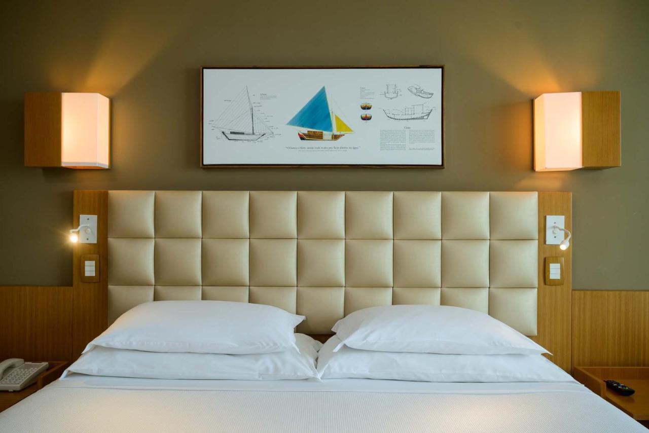 Hotel Luzeiros Sao Luis Экстерьер фото The photo shows a modern hotel room with a neatly made bed consisting of two white pillows. The headboard of the bed is upholstered in a light, padded material. Above the bed, there is a framed artwork featuring colorful sailboat illustrations, inclu