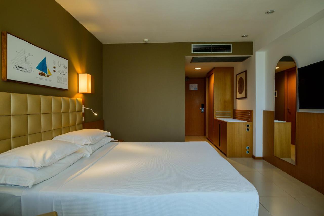 Hotel Luzeiros Sao Luis Экстерьер фото The photo shows a modern hotel room with a simple and elegant design. The room features a large bed with white linens, positioned against a beige upholstered headboard. There is a bedside lamp on one side of the bed. The walls are in soft shades, wit