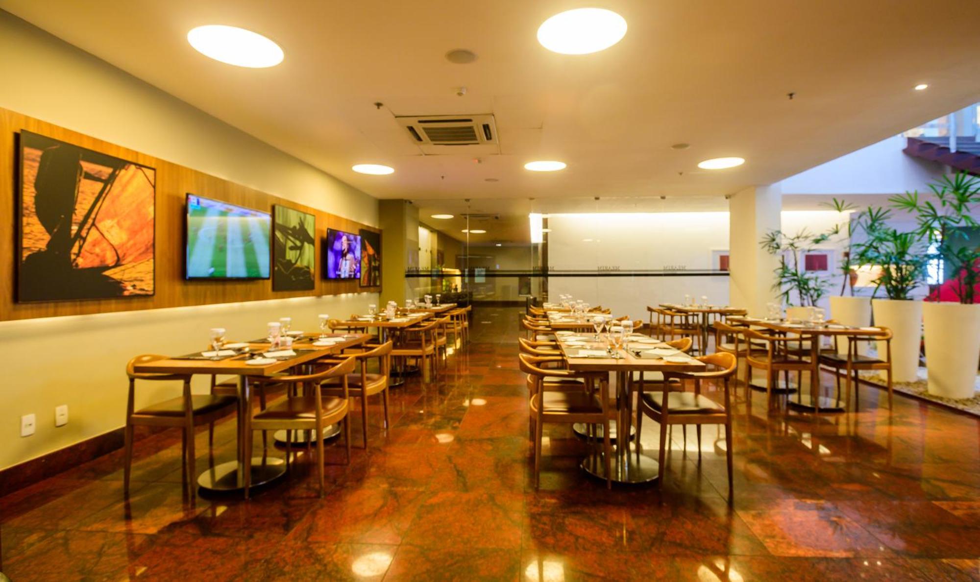 Hotel Luzeiros Sao Luis Экстерьер фото The image shows the interior of a restaurant. The space features several wooden tables and chairs arranged throughout, with table settings visible on each table. The flooring appears to be polished and reflective, possibly with a reddish-brown tone. 