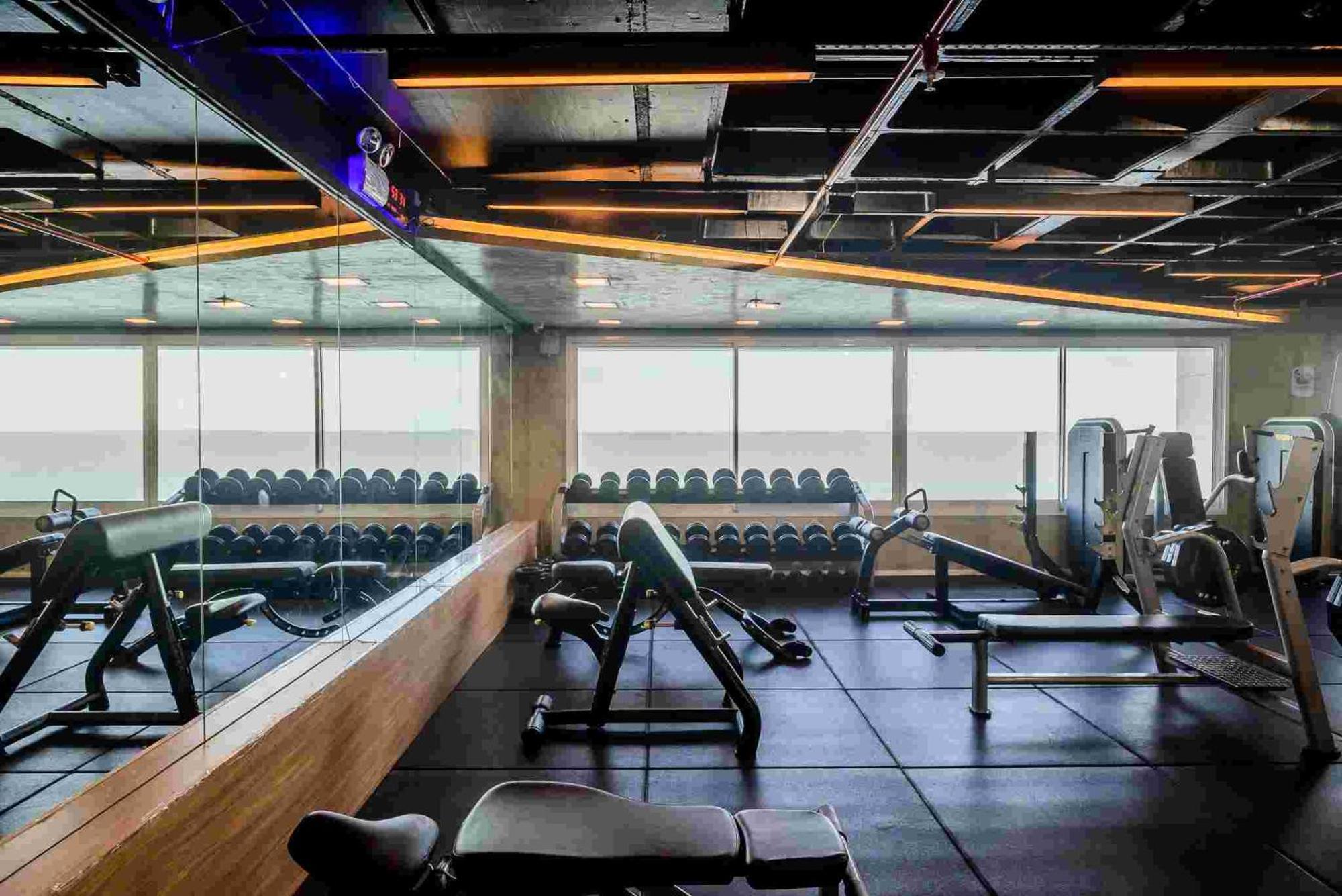Hotel Luzeiros Sao Luis Экстерьер фото The photo shows a modern gym interior. There are several fitness machines and equipment, including free weights organized on shelves, weight benches, and exercise machines. The gym features large windows, allowing natural light to enter, and has a mi