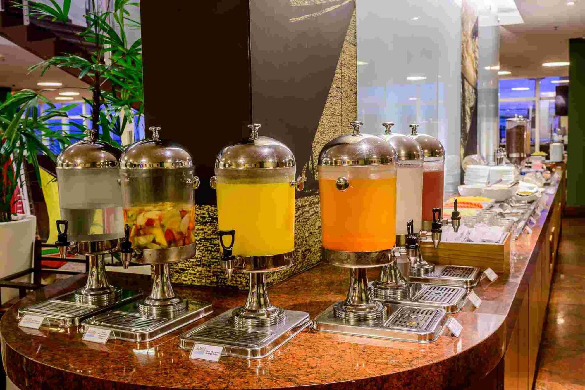 Hotel Luzeiros Sao Luis Экстерьер фото The photo shows a buffet-style beverage station with several drink dispensers placed on a polished countertop. There are six dispensers, each with a metallic design and glass body. The first dispenser contains a clear liquid, possibly water or a ligh