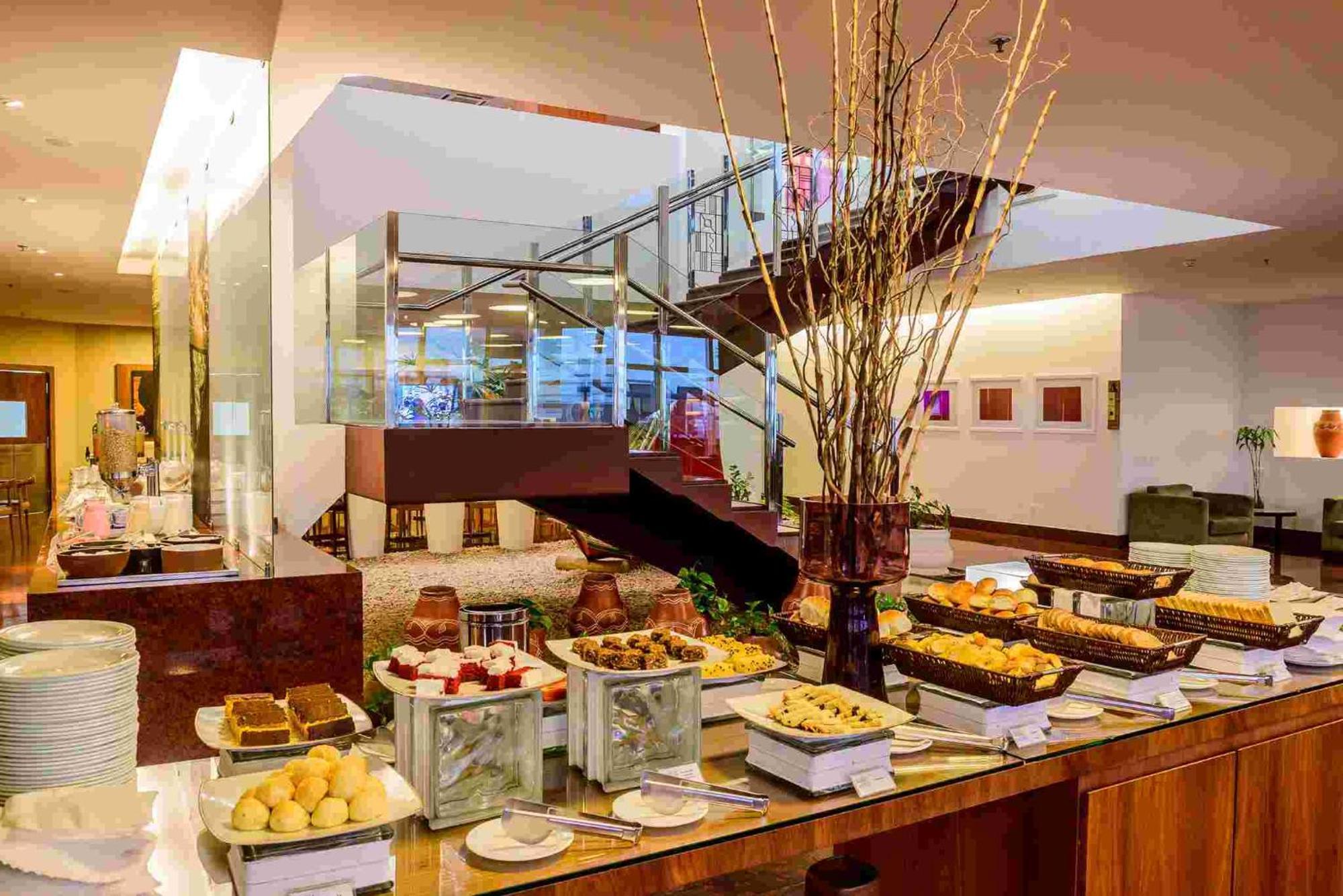 Hotel Luzeiros Sao Luis Экстерьер фото The photo depicts an elegantly arranged dining area featuring a buffet setup. There are various food items displayed on long tables, including an assortment of pastries, desserts, and fruit. Decorative elements, such as tall branches in vases, add to