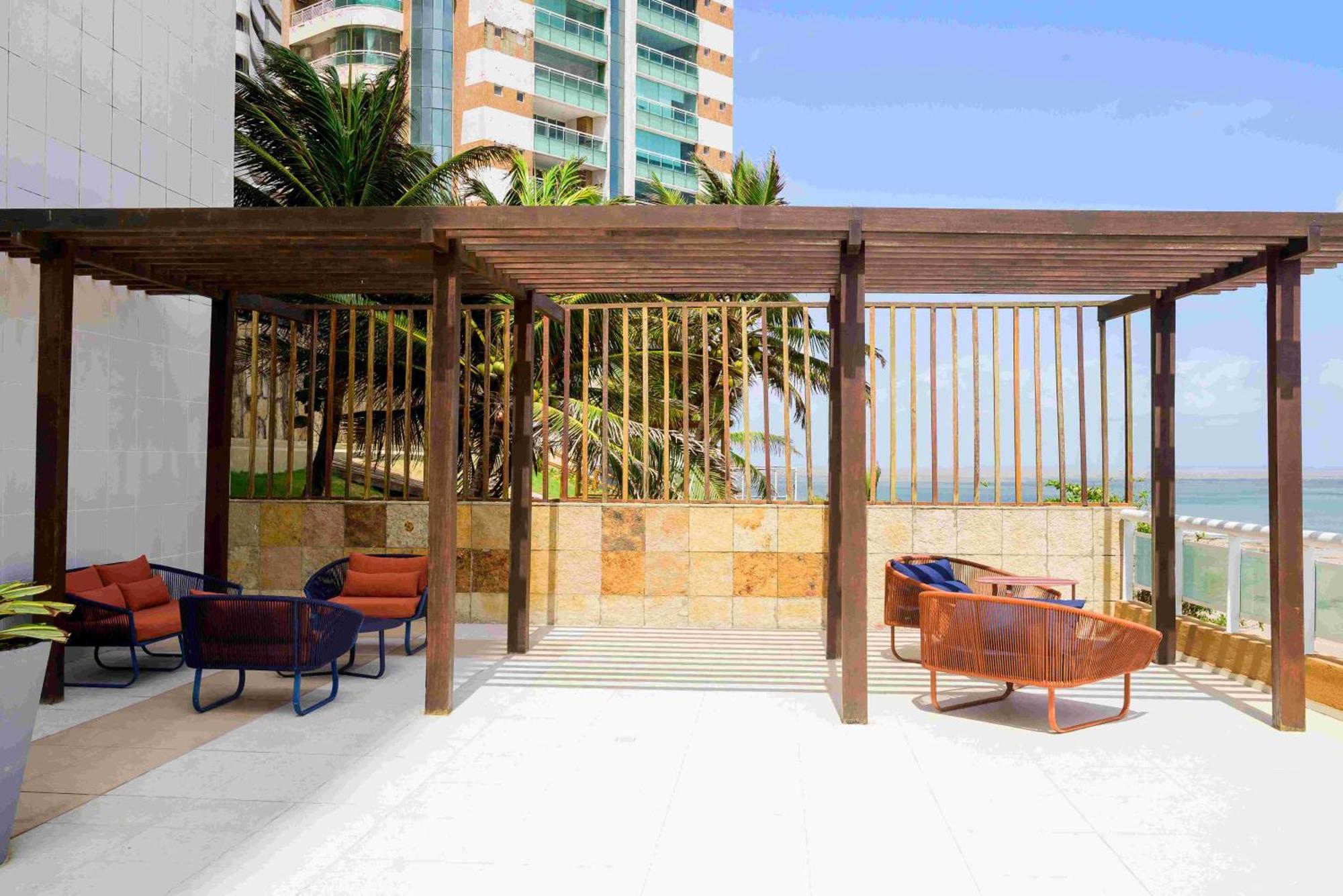 Hotel Luzeiros Sao Luis Экстерьер фото The photo shows a modern outdoor space that features a pergola structure made from wooden beams. Underneath the pergola, there are a few stylish chairs arranged for seating. The area is adorned with tropical plants, suggesting a lush environment. In 
