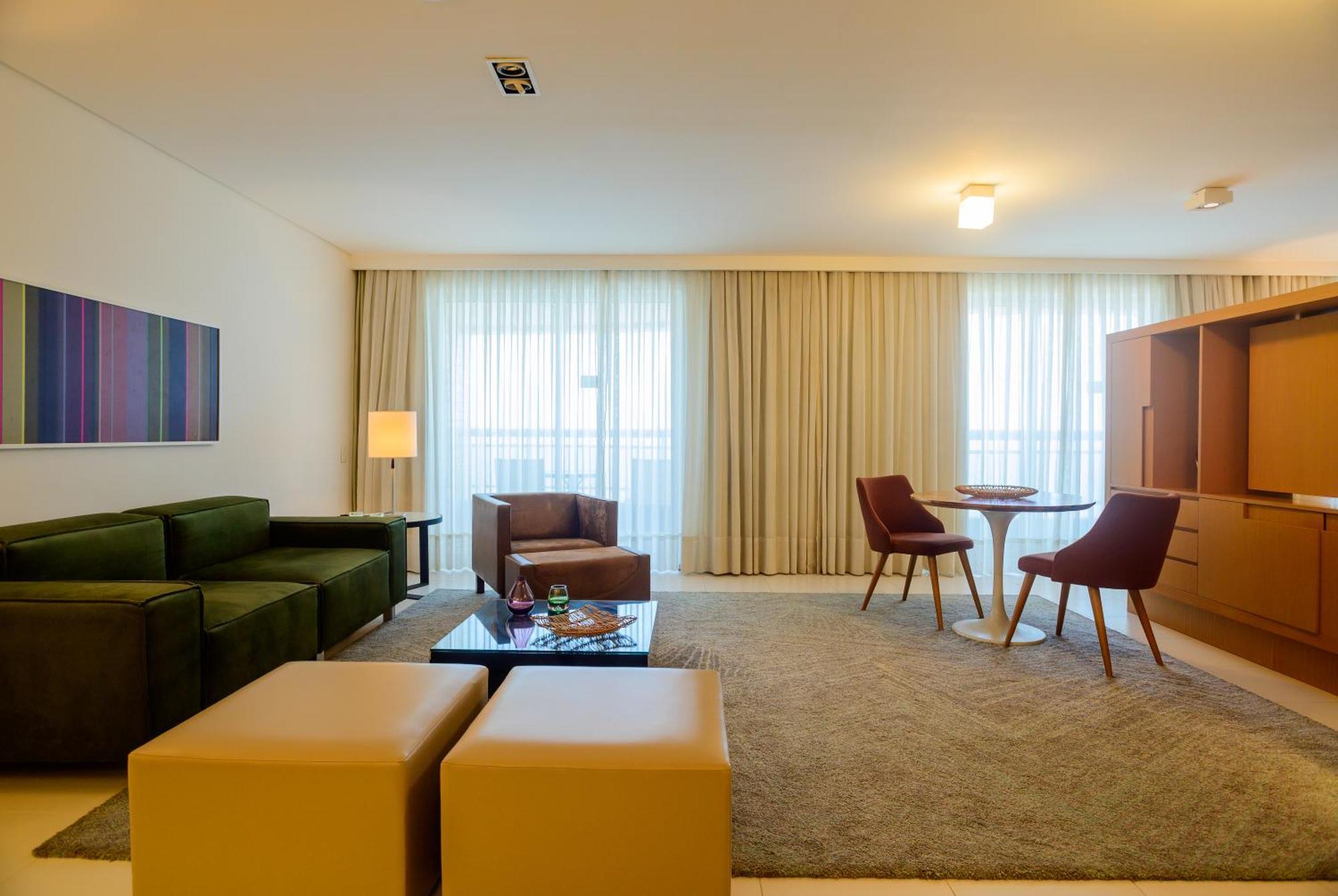 Hotel Luzeiros Sao Luis Экстерьер фото The photo depicts a modern and well-lit living space. It features a green sectional sofa and a brown armchair, with a small glass coffee table in front. There are two brown chairs around a circular table, providing a cozy dining or meeting area. The 