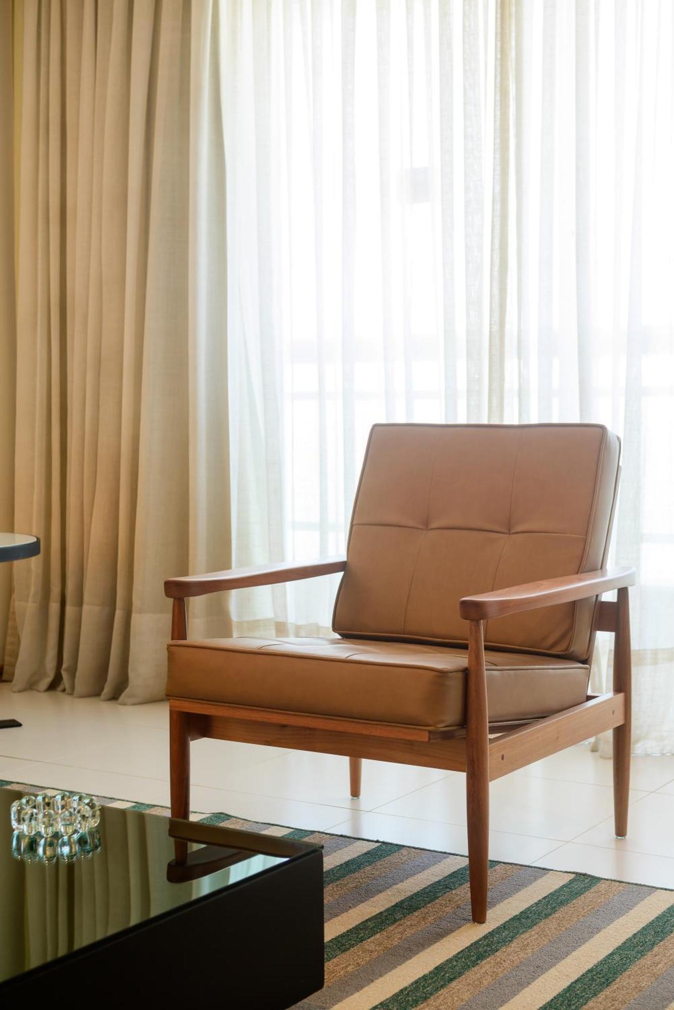 Hotel Luzeiros Sao Luis Экстерьер фото The photo shows a stylish, minimalist armchair with a simple wooden frame and a tan leather cushion. It is positioned near large curtains that allow natural light to enter the room, creating a warm and inviting atmosphere. The overall setting appears