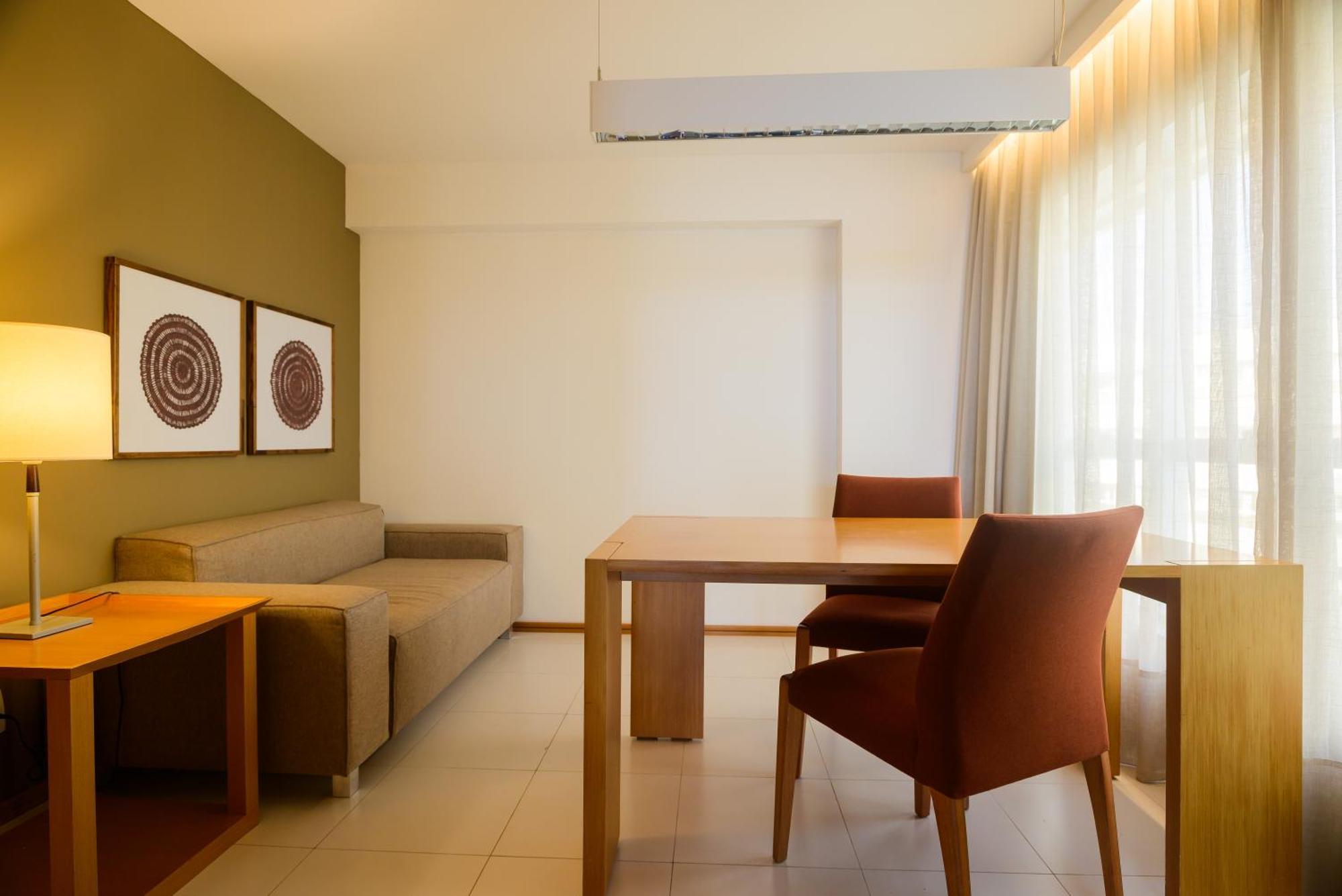Hotel Luzeiros Sao Luis Экстерьер фото The photo shows an interior space that appears to be a small living or dining area. On the left side, there is a brown sofa, and across from it, a light wooden dining table with two orange-brown chairs. The walls are painted in a soft green color, an
