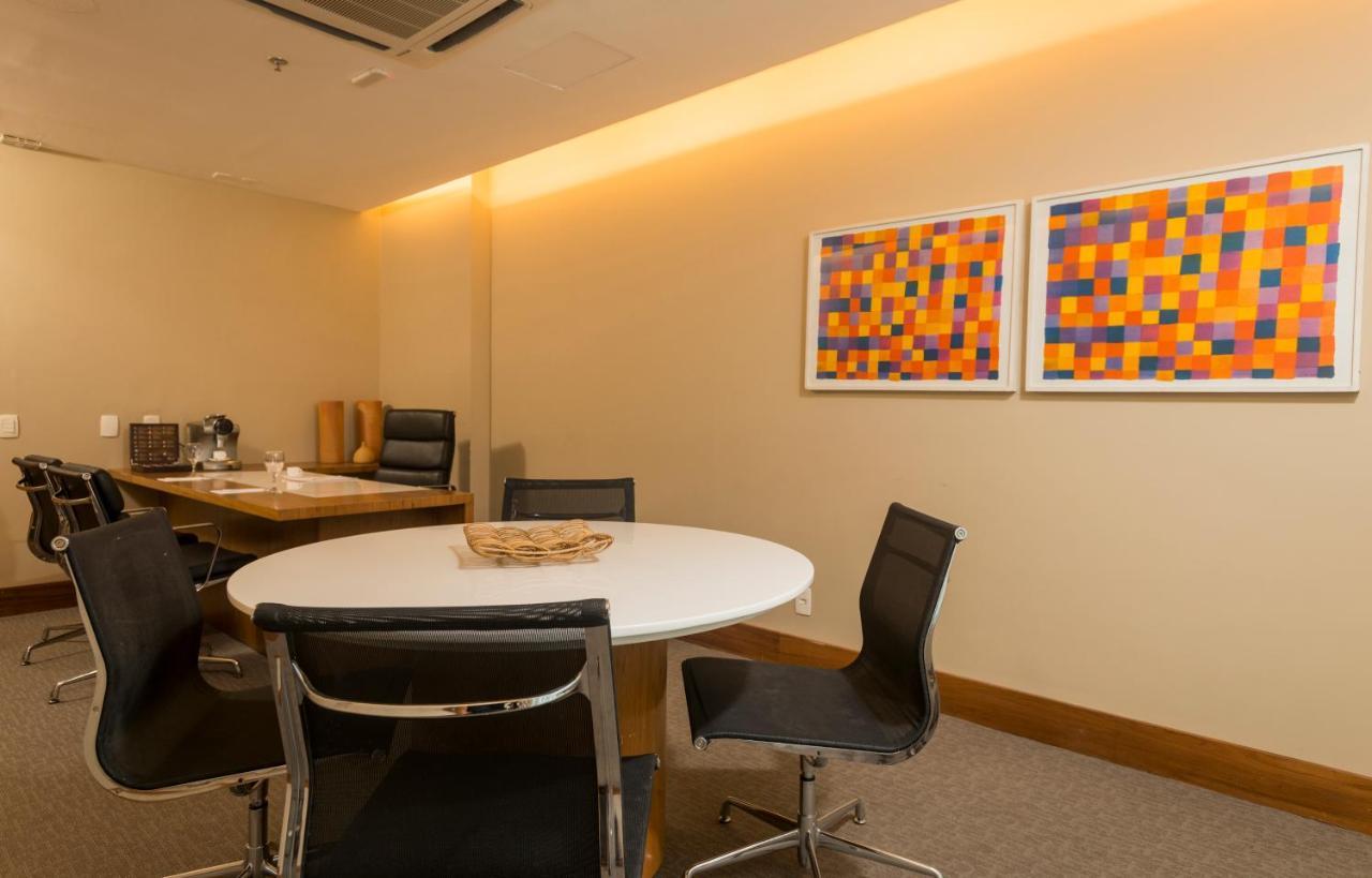 Hotel Luzeiros Sao Luis Экстерьер фото The photo shows a stylish office or meeting room with a round white table in the center, surrounded by black chairs. The walls are neutral in color, and there are two pieces of abstract art hanging on the wall, featuring vibrant squares in hues of or