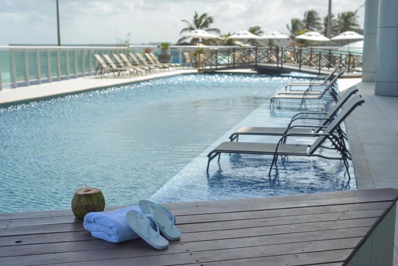 Hotel Luzeiros Sao Luis Экстерьер фото The image shows a tranquil swimming pool area. The pool has a modern design with clear blue water, surrounded by wooden decking. On one side, there are several lounge chairs arranged neatly, likely for sunbathing or relaxation. A few palm trees and u