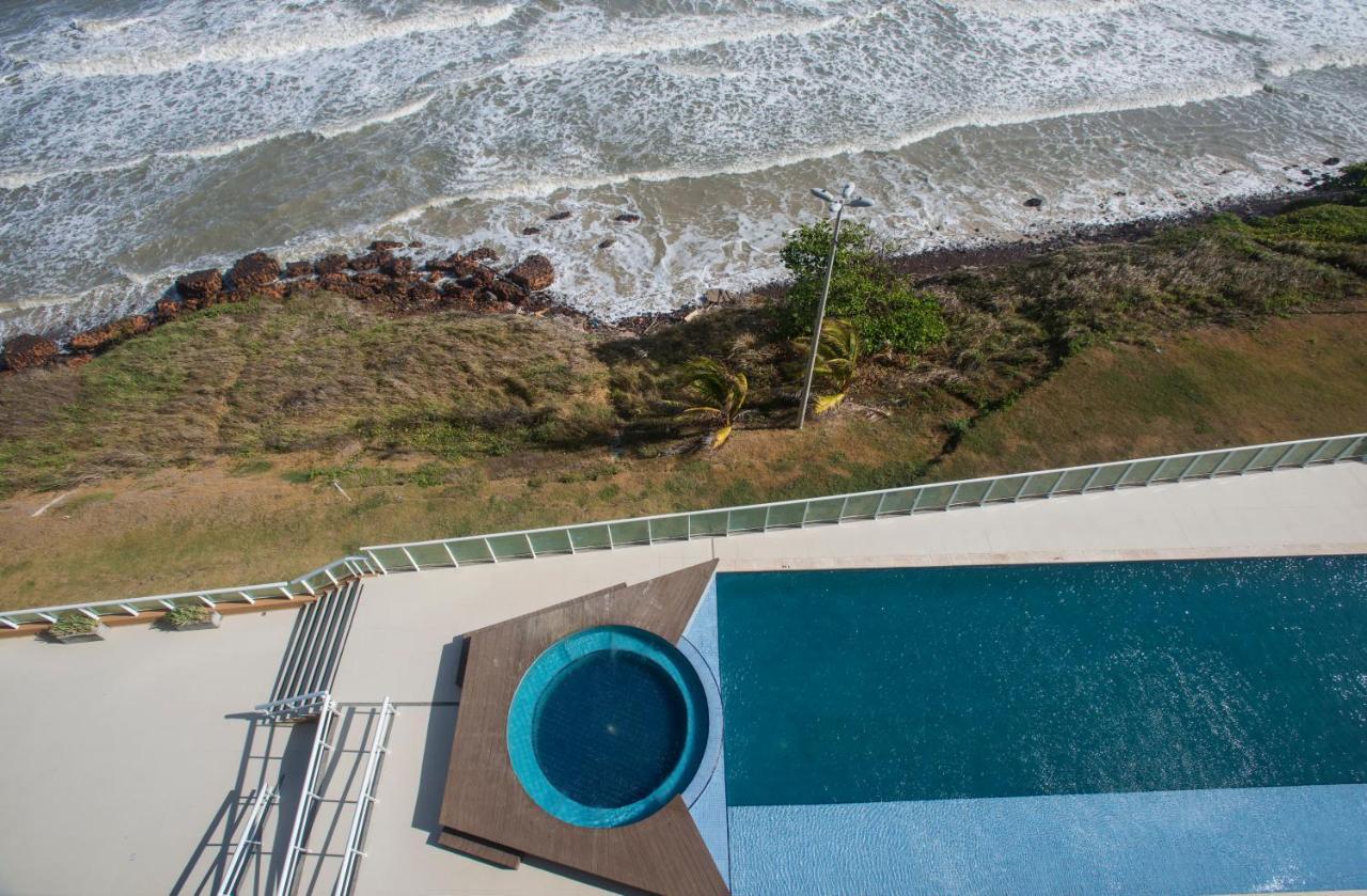 Hotel Luzeiros Sao Luis Экстерьер фото The photo shows an aerial view of a swimming pool area next to a beach. The scene includes a larger pool with a smaller circular hot tub attached to it. The pool area is surrounded by a deck, and there are some lounge chairs visible. In the backgroun