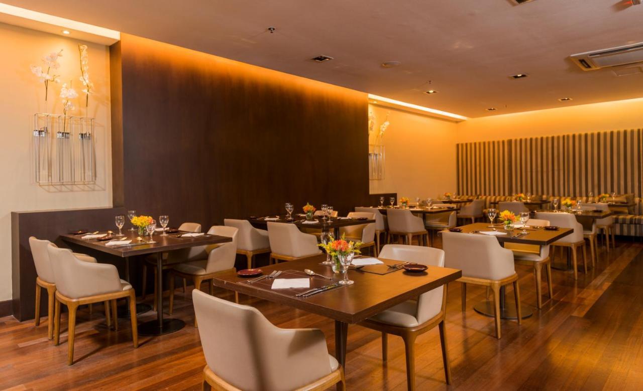 Hotel Luzeiros Sao Luis Экстерьер фото The photo shows a modern restaurant interior. There are several tables arranged with light wooden surfaces and comfortable cream-colored chairs. Each table has a flower centerpiece and is set with tableware, including wine glasses and plates. The wal