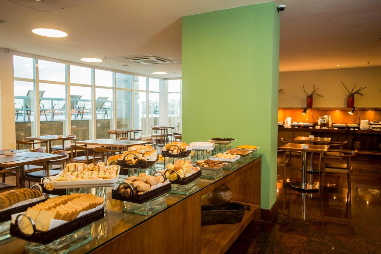 Hotel Luzeiros Sao Luis Экстерьер фото The photo shows a dining area with a buffet-style setup. On one side, there are multiple trays filled with various types of pastries and snacks, arranged neatly on a glass display. The room features large windows allowing natural light to come in, cr